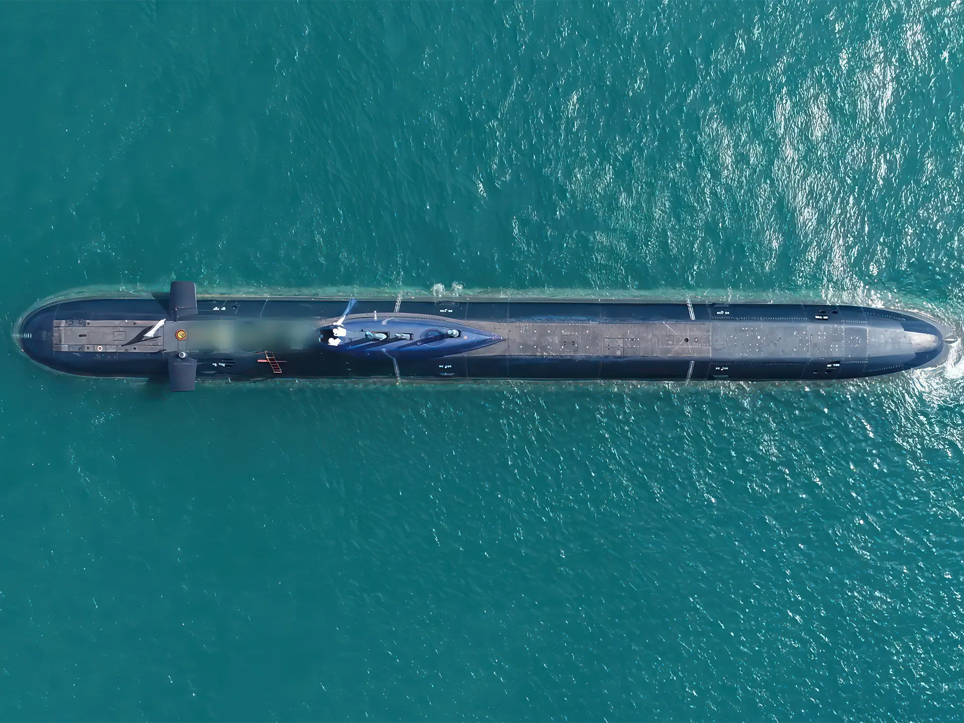 Aerial view of a long, dark submarine traveling through clear turquoise water.
