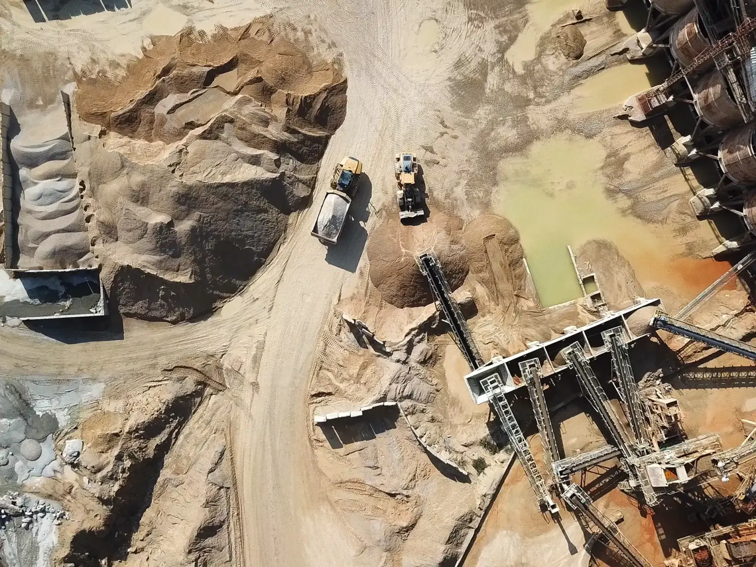 Aerial view of heavy machinery and conveyor systems operating in a sandy quarry with stockpiles of material.