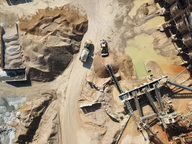 Aerial view of heavy machinery and conveyor systems operating in a sandy quarry with stockpiles of material.