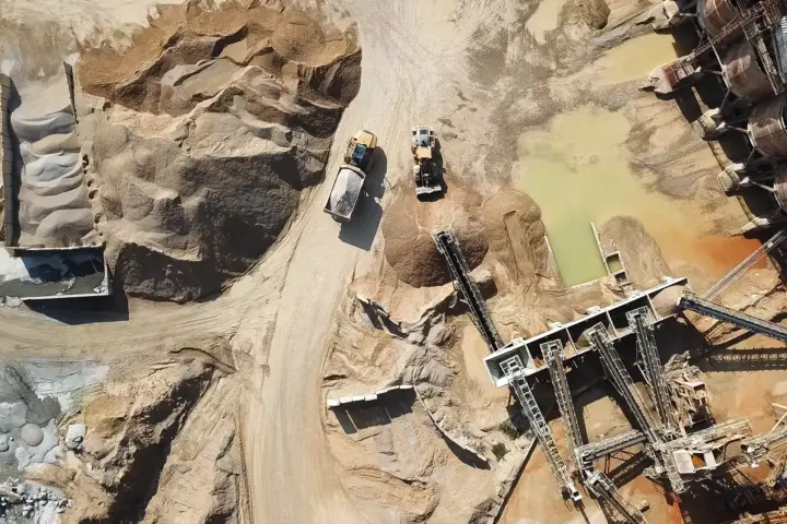 Aerial view of heavy machinery and conveyor systems operating in a sandy quarry with stockpiles of material.