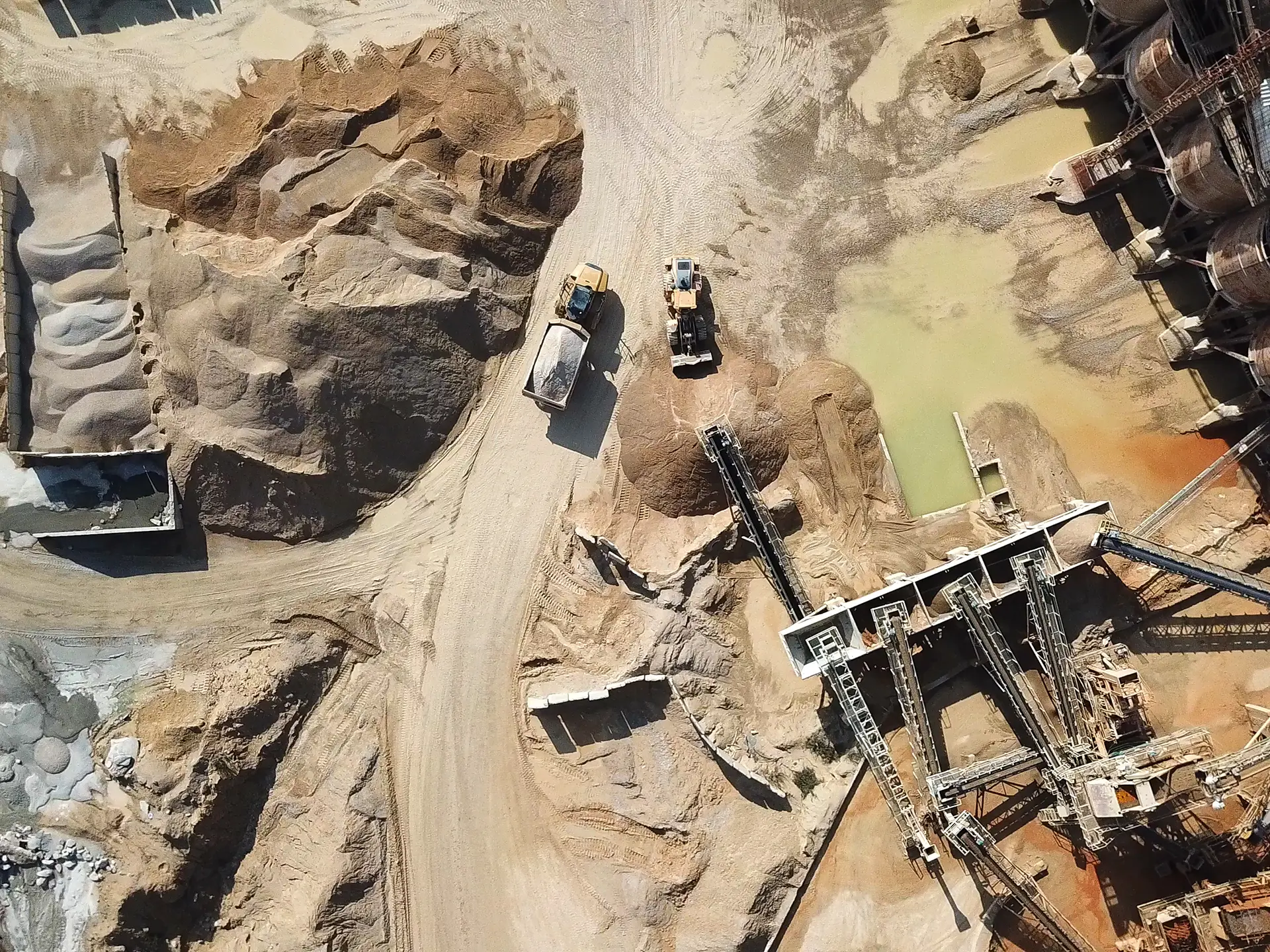 Aerial view of heavy machinery and conveyor systems operating in a sandy quarry with stockpiles of material.