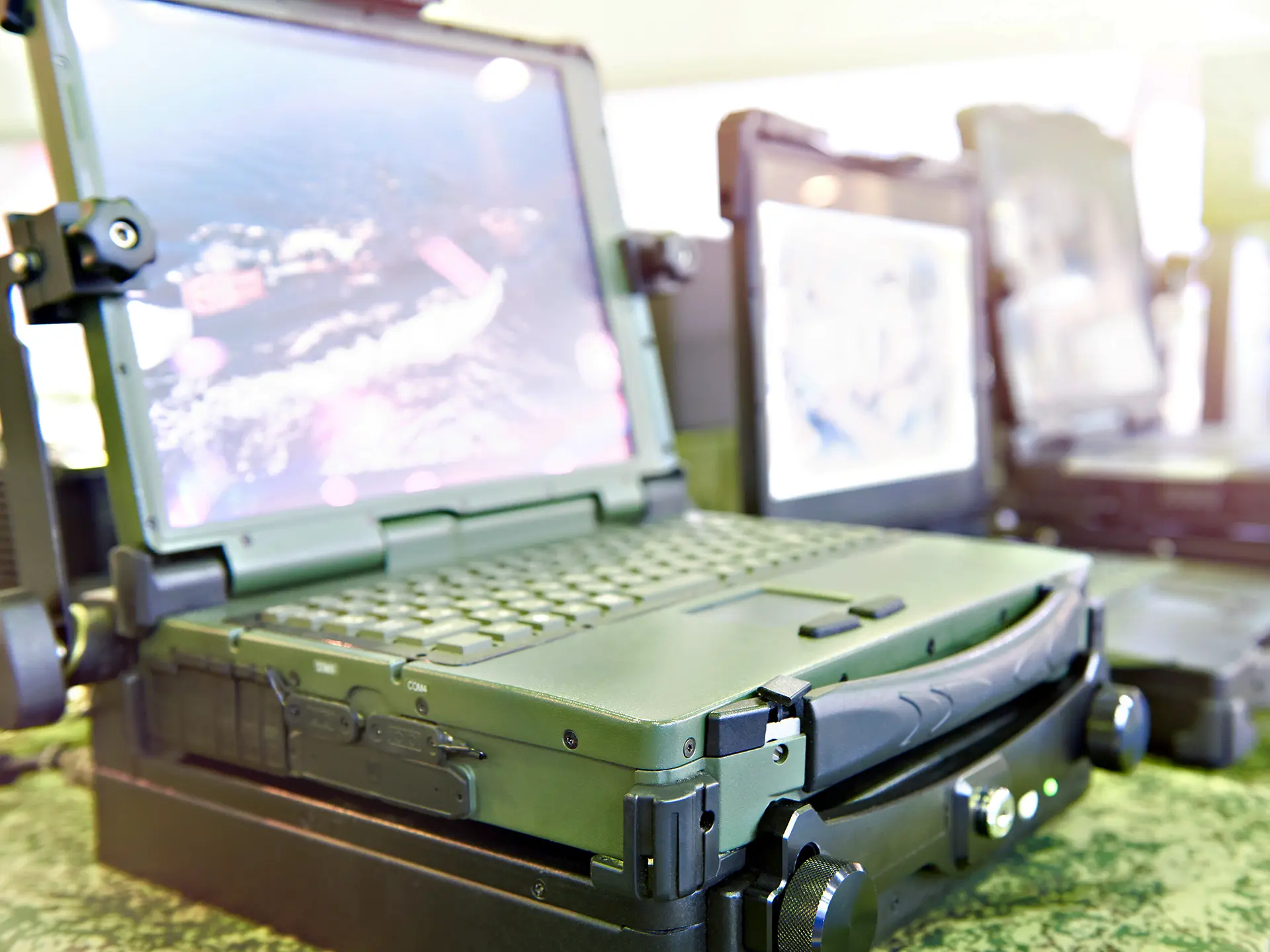 Close-up of ruggedized laptops mounted on stands, showing satellite or aerial imagery on their screens.