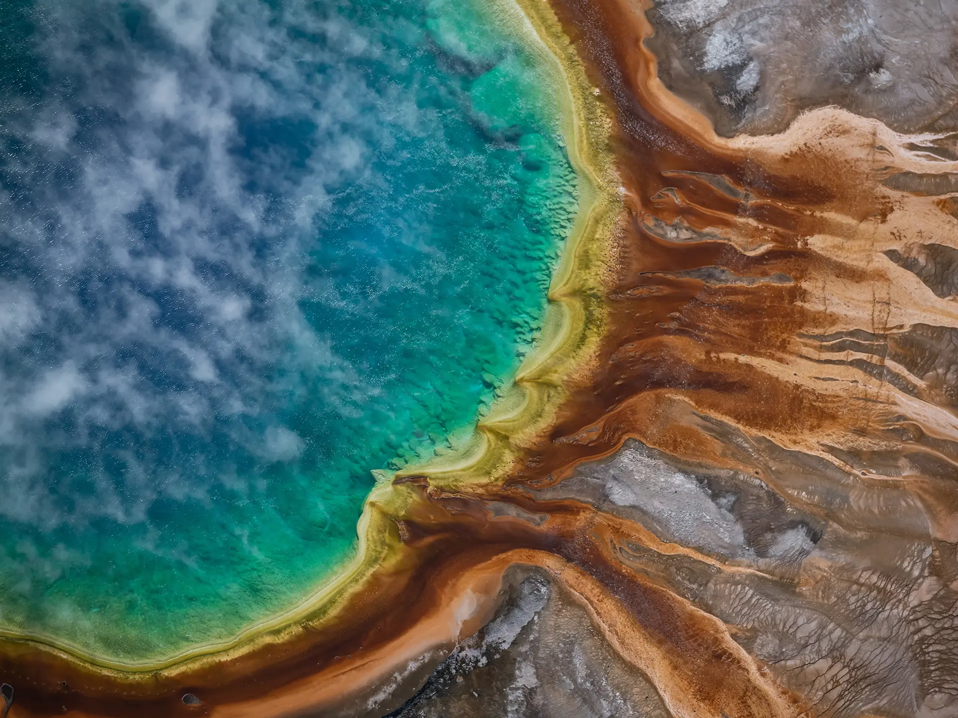 Aerial view of a vivid turquoise lake bordered by yellow and rust-colored mineral deposits and rocky terrain.