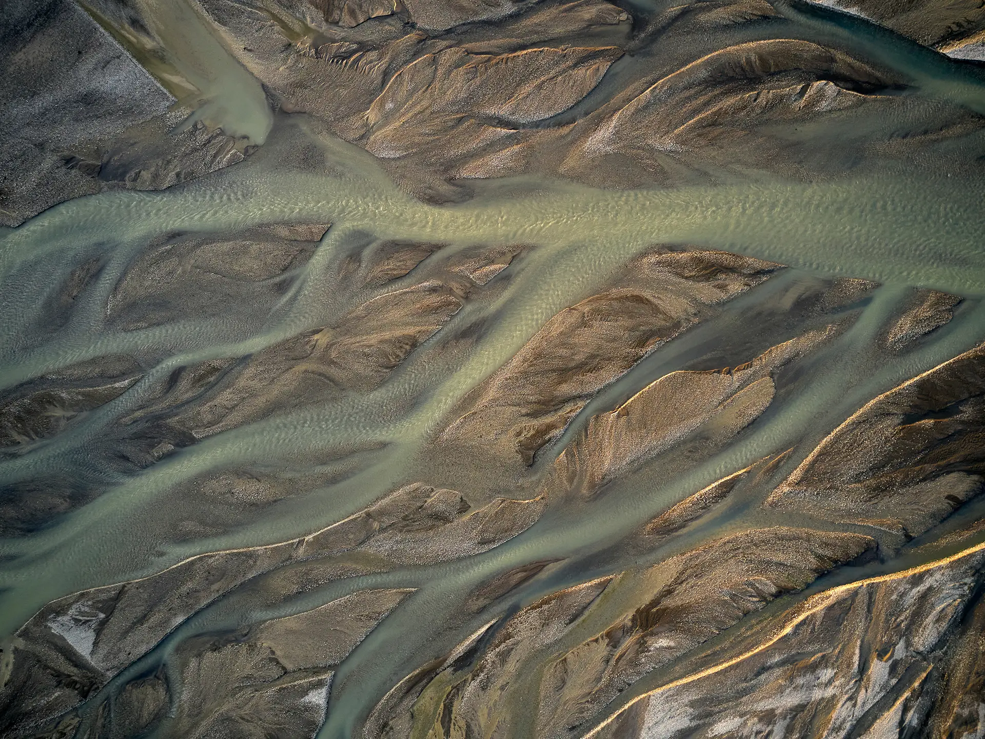 Aerial view of pale green braided river channels weaving through sandy and gravel bars.