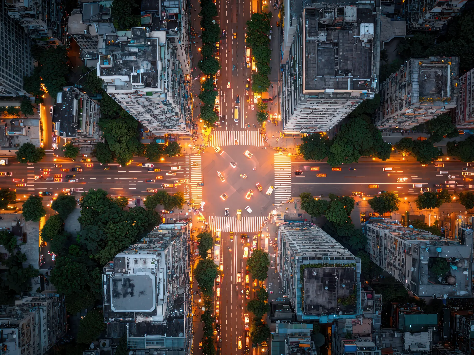 Aerial view of a brightly lit city intersection at night, with cars moving through crosswalk-lined streets surrounded by tall buildings.